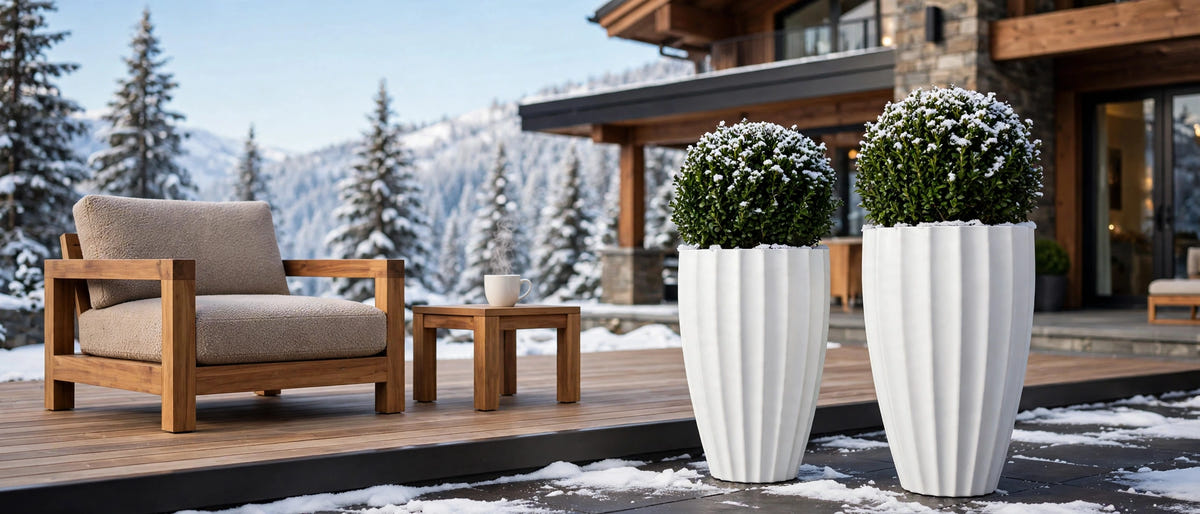 Two tall white fluted fiberglass planters holding snow-covered boxwood balls on a timber deck outside an alpine house in winter