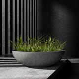 Cavo low bowl Cosapots fiberglass planter, shown planted with ornamental grasses against a slatted timber wall.