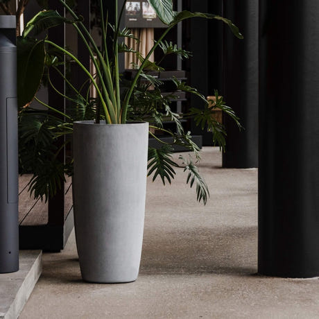 Lofto tall column Cosapots fiberglass planter, shown planted with palms in a covered walkway.