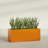 Granada rectangular fiberglass planter in Gloss Tangerine, 60 × 24 × 24 in, shown planted in a room