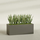 Granada rectangular fiberglass planter in Matte Bronze, 60 × 24 × 24 in, shown planted in a room